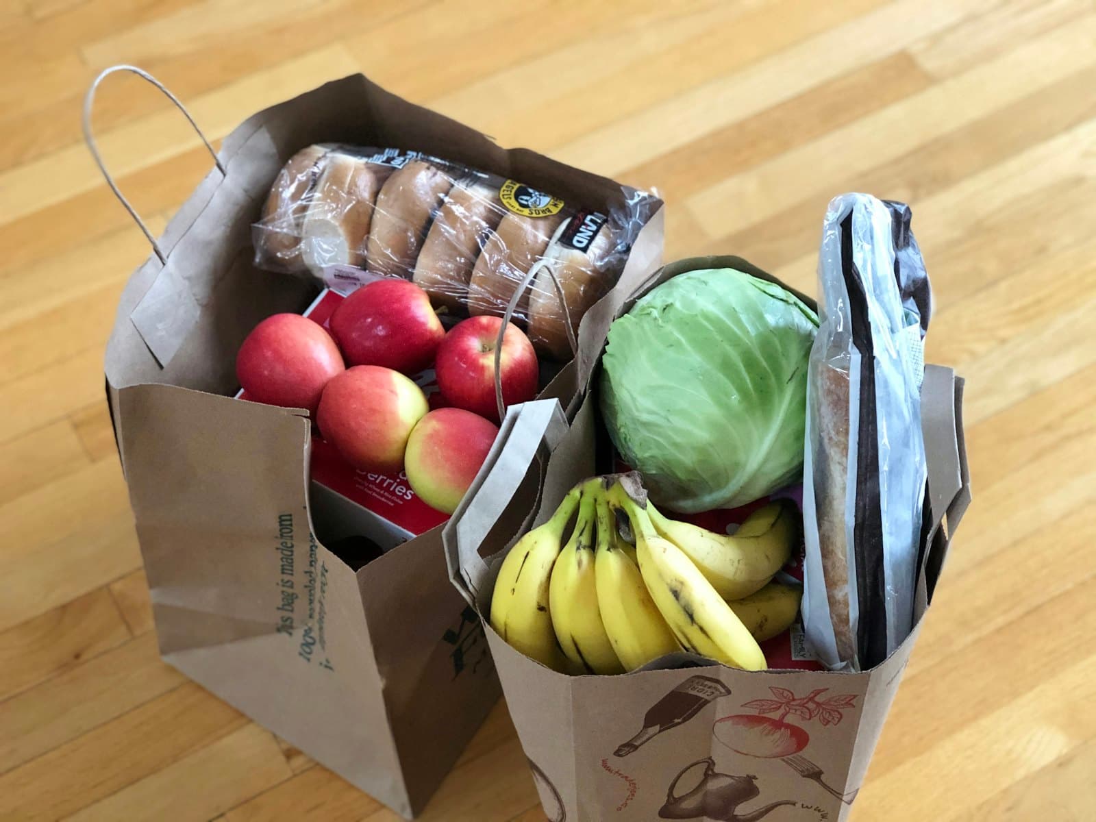 A cardboard box of fresh groceries — apples, bananas and greens.