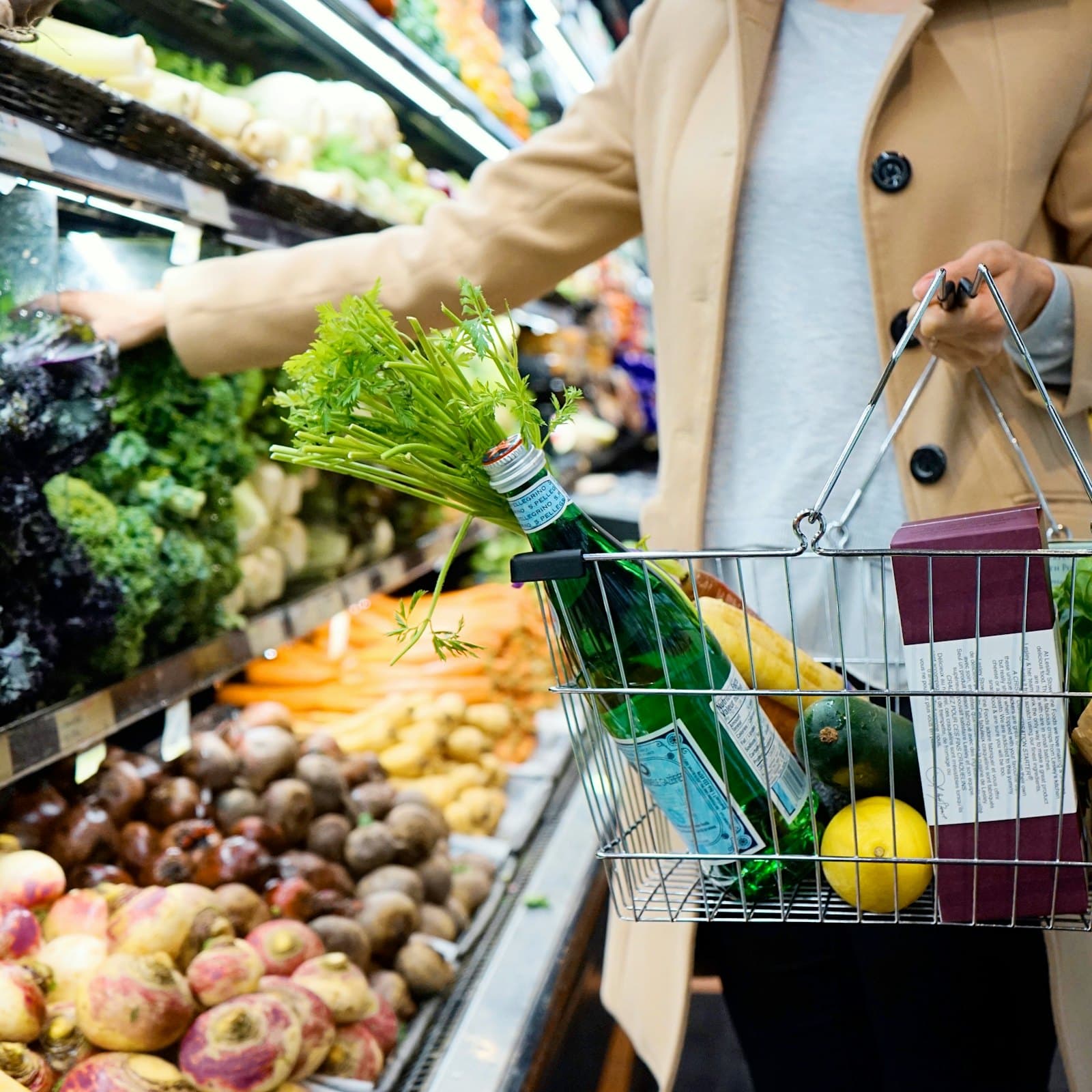 A shopper carrying a wire basket of groceries beside a produce aisle.